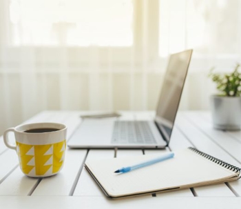 Image of a laptop drink and notepad on a desk